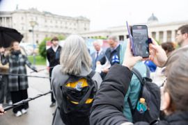 Eine Person filmt mit dem Smartphone die Pressekonferenz zur Eröffnung der Gedenkausstellung am Heldenplatz, bei der die Kooperationspartner:innen den anwesenden Journalist:innen Fragen beantworten © MKÖ/Alissar Najjar