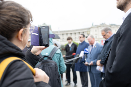Eine Person filmt mit dem Smartphone die Pressekonferenz zur Eröffnung der Gedenkausstellung am Heldenplatz, bei der die Kooperationspartner:innen den anwesenden Journalist:innen Fragen beantworten © MKÖ/Alissar Najjar