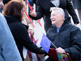 Christa Bauer begrüßt Shaul Spielmann, der eine EU-Fahne hält, Fest der Freude 2019 © MKÖ/Sebastian Philipp 