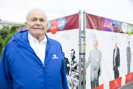 Mark Olsky, KZ-Überlebender und eines der drei "Mauthausen Babys", steht vor der Gedenkausstellung am Heldenplatz mit lebensgroßen Porträts und Zitaten von KZ-Überlebenden und Zeitzeug:innen sowie Auszügen aus dem Mauthausen-Schwur © MKÖ/Alissar Najjar