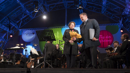 Lucia Heilmann hält den ihr überreichten Blumenstrauß und steht neben Willi Mernyi auf der Bühne. Fest der Freude 2017 © MKÖ/Sebastian Philipp  