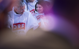 Ein Mann und eine Frau im Publikum tragen Regenponchos und lächeln einander an, Fest der Freude 2017 © MKÖ/Sebastian Philipp  